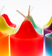 The tops of multiple candles of an assortment of colors from green, red, yellow, orange\